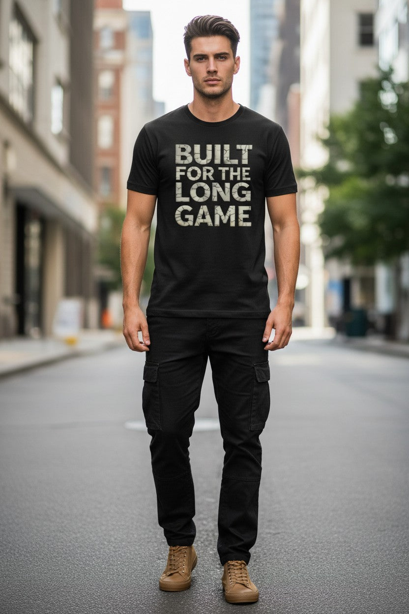 Man wearing a black t-shirt with 'BUILT FOR THE LONG GAME' text on a city street.