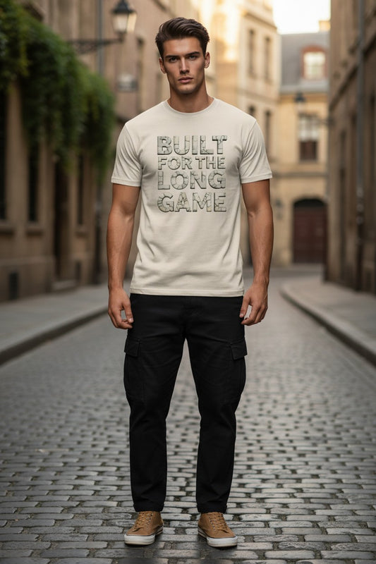 Man wearing a t-shirt with 'Built for the Long Game' text on a cobblestone street.