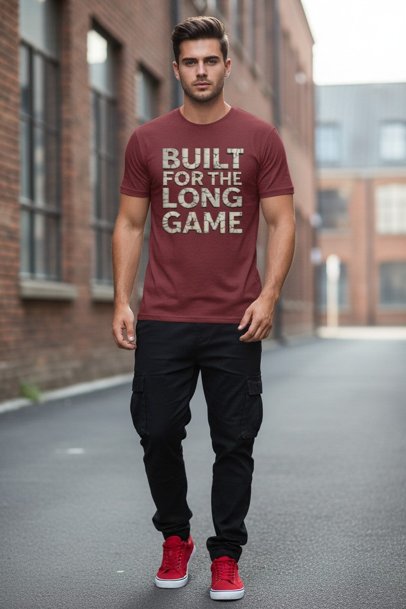 Man wearing a maroon t-shirt with 'Built for the Long Game' text, standing on a street.