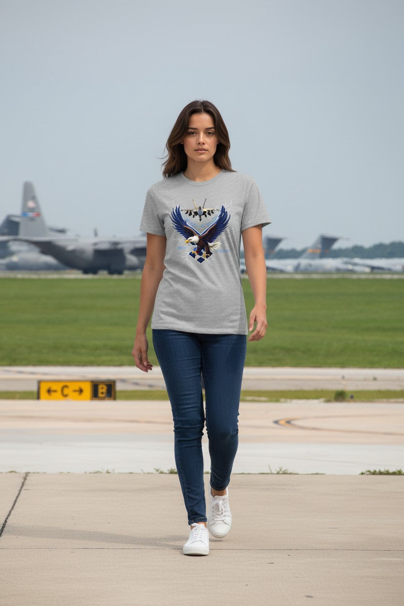 Woman wearing a gray t-shirt with an eagle design on a runway with airplanes in the background